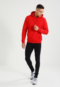 Rød hættetrøje med en frontlomme, justerbar snor og ribbede manchetter. Sæt sammen med slim-fit sorte jeans og grå sportsko.