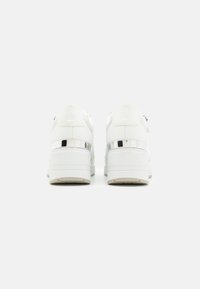 Baskets blanches avec une tige en cuir lisse, semelle blanche épaisse et accents métalliques au niveau du talon. Présente des coutures discrètes et un col rembourré.