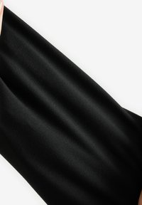 Gros plan d’une main étirant un tissu lisse, noir et texturé sur un fond blanc.