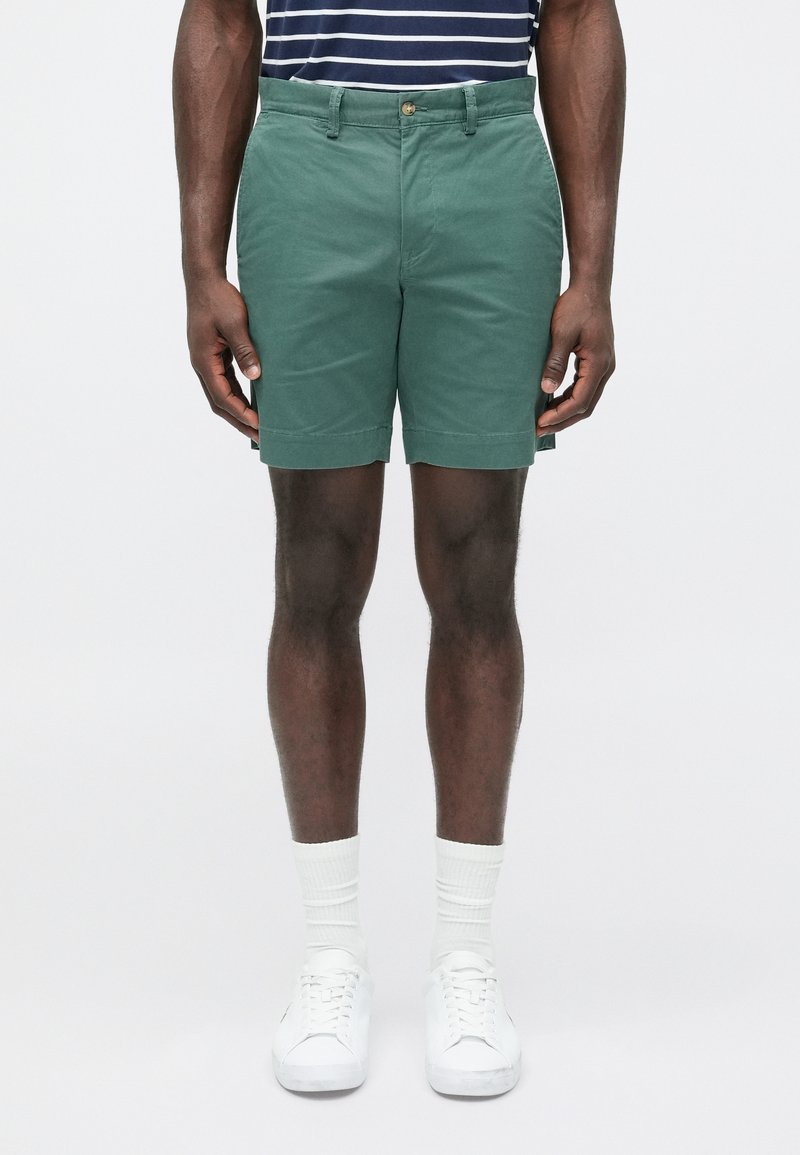 Πράσινα βαμβακερά σορτς με ίσια πρόσοψη, πλαϊνές τσέπες και γυρισμένο τελείωμα. Συνοδεύονται από λευκά αθλητικά παπούτσια και λευκές ριμπ κάλτσες.