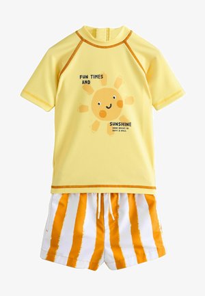 Maglia da surf gialla con maniche corte, con una grafica di un sole sorridente e del testo. Costume da bagno abbinato con strisce verticali arancioni e bianche.