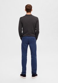 Tmavě šedá košile s dlouhým rukávem, modré kalhoty s zadními kapsami, nošené s tmavými botami. Jednoduchý, čistý design, přiléhavý střih, žádné viditelné vzory.