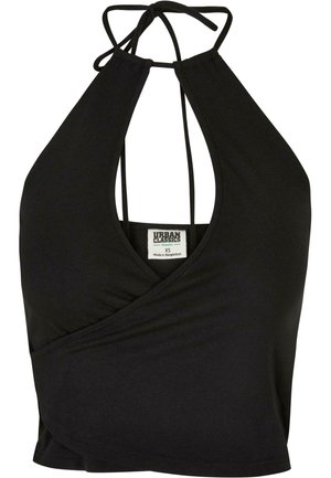 Kobieta ubrana w czarny top typu halter i czarne spodenki z białymi kwiatowymi wzorami, stojąca z jedną ręką w kieszeni i czarnych sandałach.