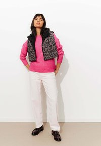 Un pull en tricot rose associé à un gilet noir à imprimé léopard, un pantalon blanc texturé et des mocassins noirs. Éléments de design simples et modernes.