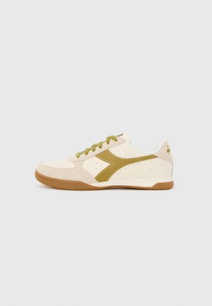 Sneakers con tomaia color crema, accenti verde oliva e suola in gomma color caramello. Presentano perforazioni e un design laterale curvo.