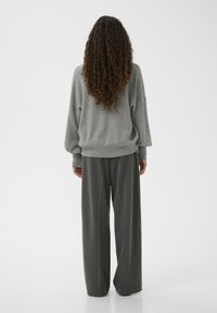 Grå oversize sweatshirt med sänkta axlar, bärs med vida grå byxor. Tyget verkar mjukt med en texturerad finish.