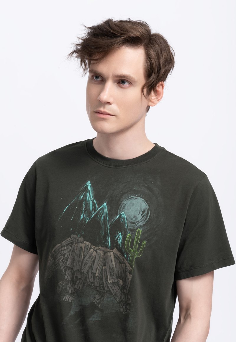 Donkergroene katoenen t-shirt met een afbeelding van bergen, een maan en een cactus in tinten blauw en bruin. Zachte textuur, klassieke pasvorm.