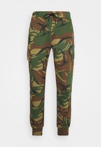 Kamouflagebyxor i gröna, bruna och svarta nyanser. Har ett elastiskt midjeband med justerbar dragsko och sidofickor.