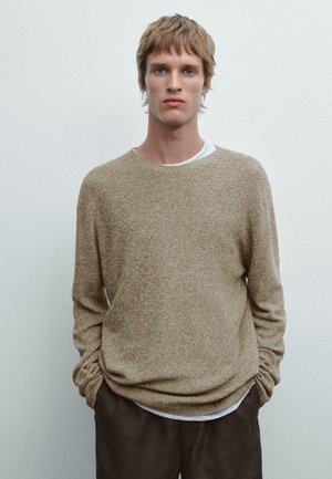 Beige textured sweater with a crew neckline, worn over a white layered shirt. Slim fit and long sleeves, paired with dark trousers.