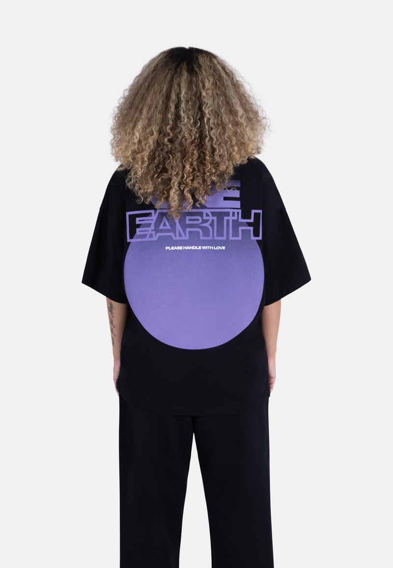 Svart oversized t-skjorte med en lilla sirkulær grafikk og tekst på baksiden som sier "REDDE JORDEN" og "VENNLIGST HÅNDTER MED KJÆRLIGHET."