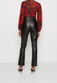 Pantalon en cuir noir avec une coupe slim et des détails de couture subtils ; associé à un chemisier floral rouge transparent et des sandales à talons noires.