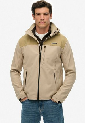 Beige softshell jacket with a hood, brown shoulder accents, zippered chest pocket, long sleeves, and two side pockets.