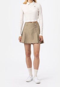 Bílý dlouhý rukáv, zkrácená polo košile s knoflíky, v kombinaci s khaki skládací sukní se štítkem, bílými ponožkami a bílými teniskami.