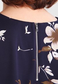 Navy floral dress with a smooth fabric, featuring a visible metallic zipper at the back and a round neckline. Subtle color accents in gold and white.