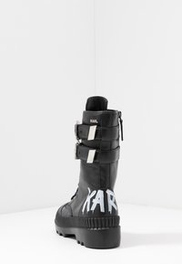 Bota de combate de cuero negro con diseño acolchado, dos correas con hebillas plateadas, suela gruesa de goma y texto blanco "KARL" en el talón.