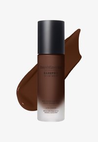 Matte vloeibare foundation in een donkerbruine fles met een zwarte dop. Ernaast een bruine kleurstaal van het product. SPF 20 staat op de voorkant vermeld.