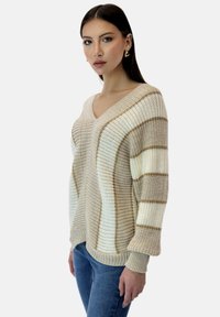 Suéter de punto rayado en beige y crema con escote en V, tejido texturizado, mangas globo y puños acanalados. Combinado con jeans azules.