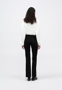 Hanorac alb cu croială lejeră și umeri căzuți, asortat cu blugi negri de tip slim-fit. Model care poartă pantofi negri, văzut din spate.