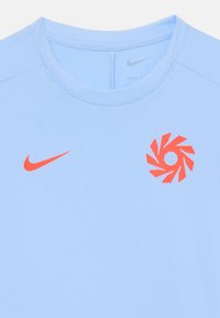 Svijetloplava Nike sportska majica s okruglim izrezom, koja ima narančasti Nike swoosh i spiralni logo dizajn na grudima. Glatka tekstura.