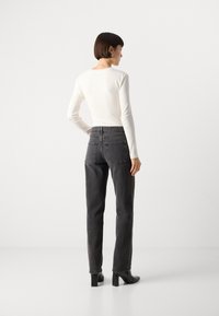 Jeans gris slim avec taille haute et poches arrière, associés à un haut ajusté à manches longues en ribbed blanc. Chaussures à talons blocs noires.