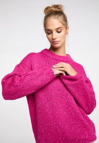 Maglione chunky a maglia in un vibrante rosa, con scollo rotondo, maniche lunghe e una finitura strutturata con sottili macchie sparse.