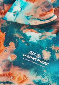 Un sweat à capuche présentant un motif tie-dye coloré dans des tons de bleu, orange et blanc. Comprend un graphisme de texte en blanc : "Avenir Créatif" et le logo de la marque.