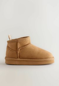 Bottine en suède beige avec un bout arrondi, des coutures texturées sur le côté et une petite boucle en tissu à l'arrière pour faciliter l'enfilage. Semelle en caoutchouc.