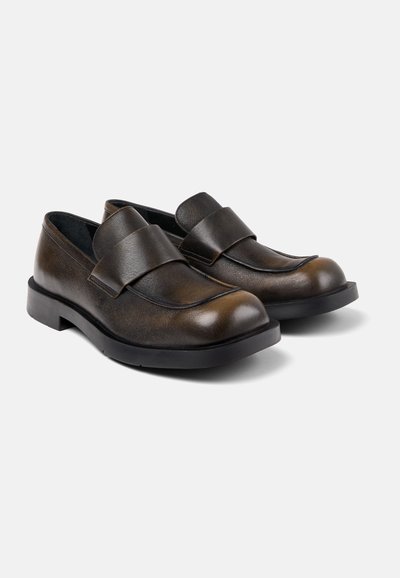 Brown leather slip-on shoes with a rounded toe, padded front strap, and a thick black rubber sole. Textured finish on the upper.