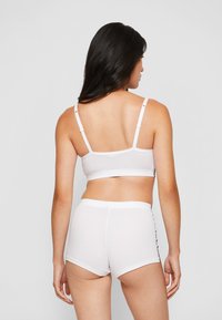 Bralette branca de algodão com alças finas e calções brancos a condizer. Ambos têm uma textura suave e um design simples e sem costuras.