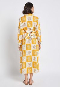 Long, light-colored dress with a yellow and white block pattern featuring floral designs. Tied waist and buttoned cuffs. Soft fabric.
