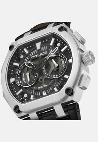 Silverfärgad rostfri klocka med svart urtavla, dubbeltidsvisning, oktagonal klockkropp och svart gummiband. Noterbara chronografdetaljer ingår.