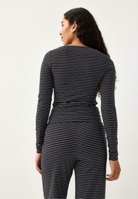 Maglietta a maniche lunghe con stretti righe bianche e nere, caratterizzata da uno scollo rotondo e una texture liscia. Indossata con pantaloni coordinati a motivo.