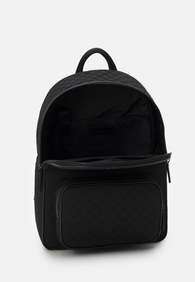 Sac à dos matelassé noir avec un grand compartiment principal et une poche avant zippée ; il dispose d'une poignée supérieure et de bretelles ajustables.