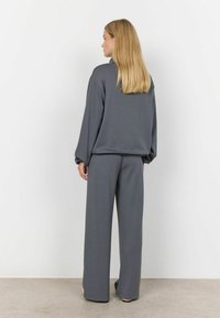 Grijs loungewear-set met een losse lange mouwtop en wijde broekspijpen. Zacht materiaal met een minimale textuur en een elastische tailleband.