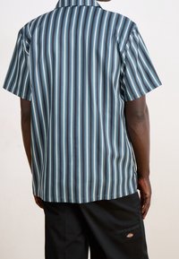 Camisa de botones de manga corta con rayas verticales en azul, negro y blanco, hecha de una tela suave, con cuello estándar y un corte relajado.