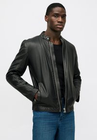 Musta nahkatakki, jossa on pystykaulus, vetoketjusuljenta ja slim fit -malli. Ominaisuuksiin kuuluu sileä tekstuuri ja vähäiset ompeluyksityiskohdat.