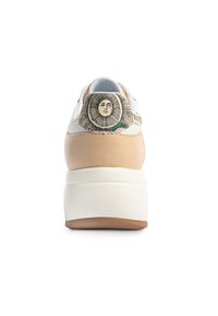 Sneaker med en beige läderkropp, vit platt formsula och en dekorativ häl med ett solmotiv och blommönster.