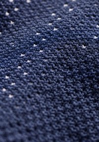Marineblauer Strickstoff mit einer strukturierten Oberfläche, der kleine weiße Punkte aufweist, die in einem Muster angeordnet sind. Das Material wirkt weich und strapazierfähig.