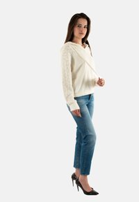 Maglione lavorato a maglia color avorio con cappuccio, caratterizzato da motivi testurizzati sulle maniche. Abbinato a jeans azzurri chiari e scarpe con tacco nere.