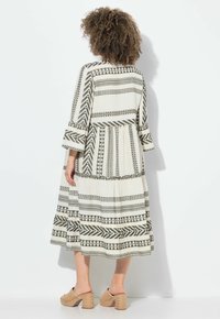 Vestido largo y fluido en crema con patrones geométricos en negro. Presenta mangas acampanadas y un diseño en capas. Combinado con sandalias de plataforma tejidas.