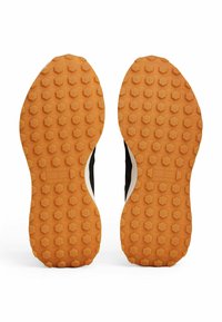 Zapatillas deportivas negras con una suela de goma naranja texturizada con un patrón hexagonal y acentos blancos a lo largo de los lados.