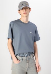 Grå bomull T-shirt med kort ärm och en liten logotyp. Tillsammans med ljusblå, något slitna denimjeans.