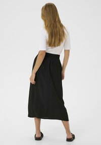 Svart, ankellång kjol med elastiskt midjeband, tillverkad i lätt tyg. Bärs med en figurnära vit topp och svarta sandaler.