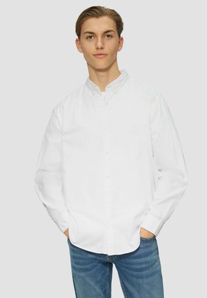 Weißes Hemd mit langen Ärmeln aus Baumwolle. Mit einem Kragen versehen und wird mit blauen Jeans kombiniert. Einfaches, klassisches Design.