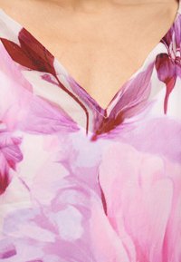 Λαιμόκοψη σε σχήμα V ενός ελαφρού, διαφανούς μπλουζιού με ροζ και μαρόν floral σχέδιο κοντά στην κλείδα.