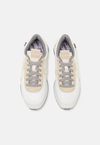 PUMA tenisky s béžovým a bílým syntetickým svrškem, šedými tkaničkami, texturovanými panely a vzorovanou stélkou, navržené pro pohodlí.