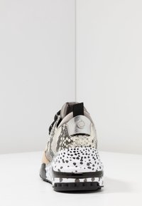 Baskets sportives avec une tige en imprimé serpent texturé, des lacets noirs et une semelle blanche et noire tachetée. Présente un accent argenté sur le talon.