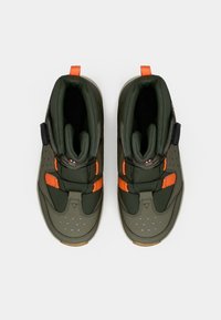 Une paire de chaussures de sport vertes et oranges avec des molettes de fixation noires, vue de dessus sur un fond blanc.