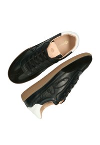 Zwarte leren sneakers met een tan rubberen zool, witte hiel details en een textuur oppervlak. Bevat veters en een logo aan de zijkant.