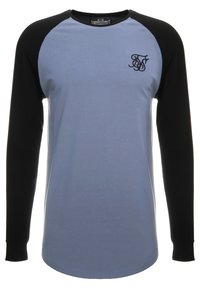 Chemise à manches longues avec un corps bleu clair et des manches raglan noires. Logo brodé remarquable sur la poitrine. Fabriquée en tissu doux.